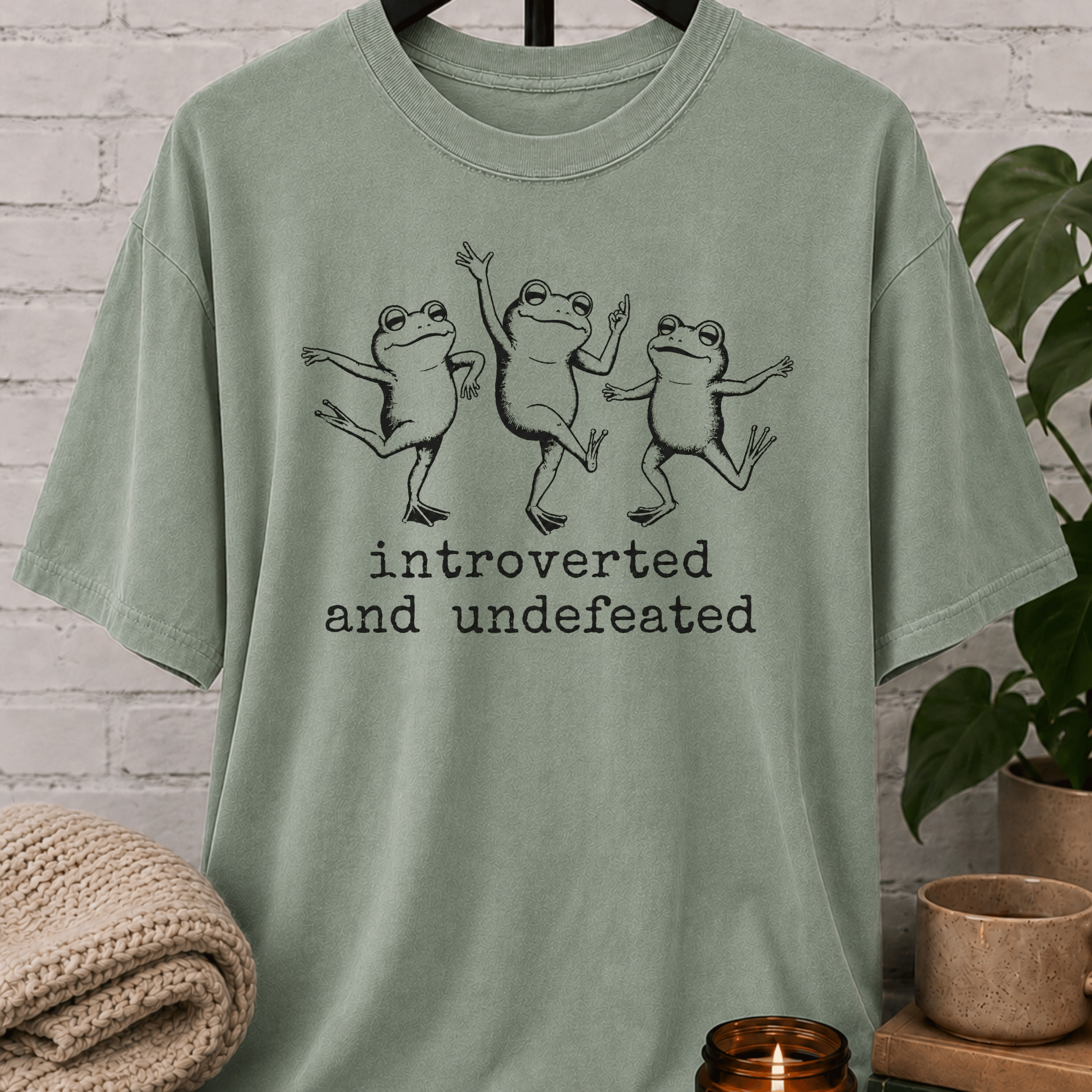Funny introvert frog T-shirt featuring three dancing frogs and the phrase “Introverted and Undefeated,” a quirky graphic tee for introverts, homebodies, quiet people, and socially awkward humor fans.
