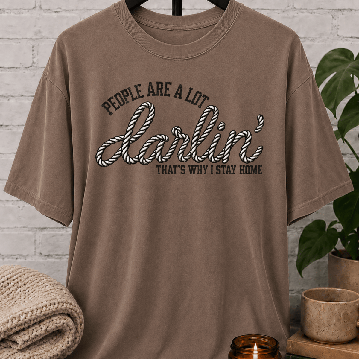 Western homebody T-shirt featuring rope-style lettering and the phrase “People Are a Lot Darlin’ That’s Why I Stay Home,” a funny sarcastic graphic tee for introverts, antisocial personalities, and stay-home lovers.