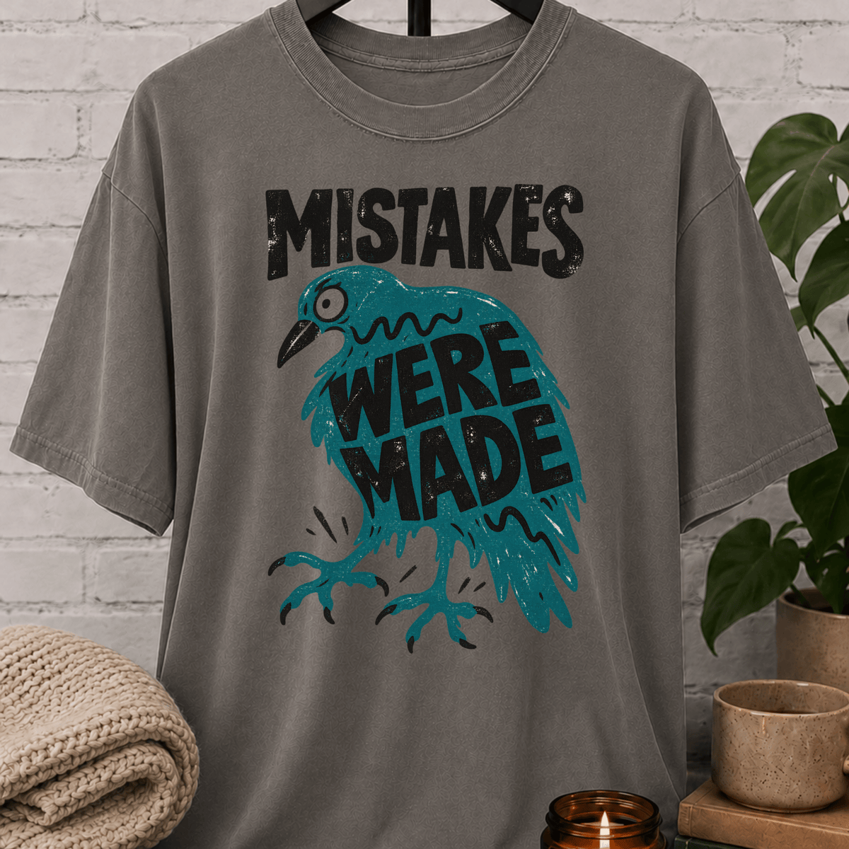 Funny crow graphic T-shirt featuring a frazzled teal bird with the phrase “Mistakes Were Made,” a sarcastic overthinker shirt for socially awkward humor and relatable mistake lovers.
