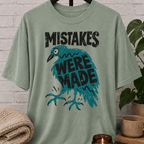 Funny crow graphic T-shirt featuring a frazzled teal bird with the phrase “Mistakes Were Made,” a sarcastic overthinker shirt for socially awkward humor and relatable mistake lovers.