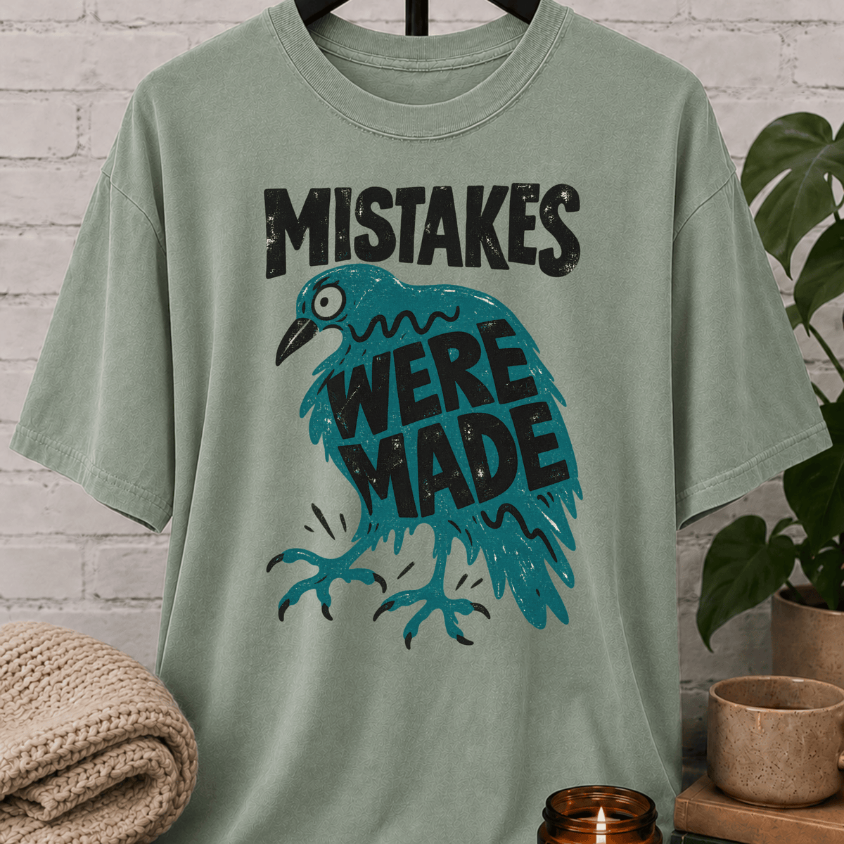 Funny crow graphic T-shirt featuring a frazzled teal bird with the phrase “Mistakes Were Made,” a sarcastic overthinker shirt for socially awkward humor and relatable mistake lovers.