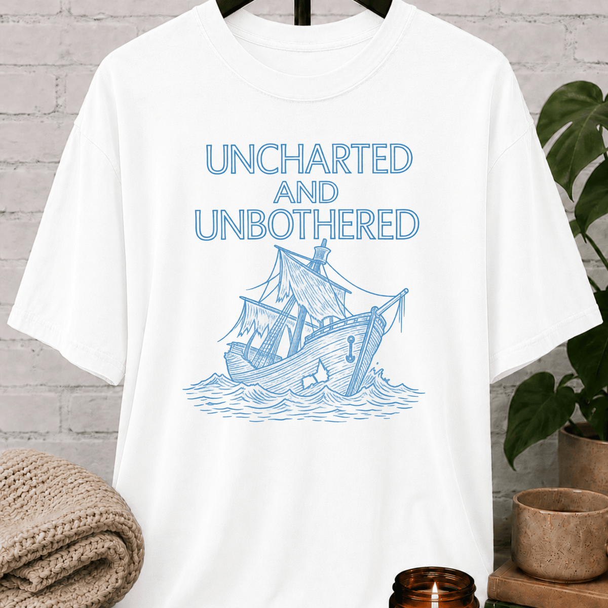 Nautical graphic T-shirt featuring a vintage sailing ship and the phrase “Uncharted and Unbothered,” a coastal graphic tee for introverts, homebodies, and lovers of ocean-inspired humor.