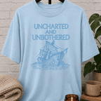 Nautical graphic T-shirt featuring a vintage sailing ship and the phrase “Uncharted and Unbothered,” a coastal graphic tee for introverts, homebodies, and lovers of ocean-inspired humor.