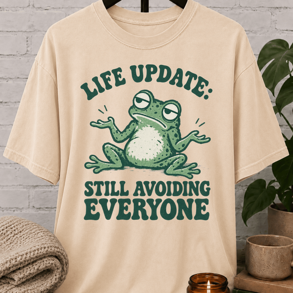 Funny introvert frog T-shirt featuring a shrugging frog and the phrase “Life Update Still Avoiding Everyone,” a sarcastic avoid people graphic tee for socially selective and low social battery humor fans.