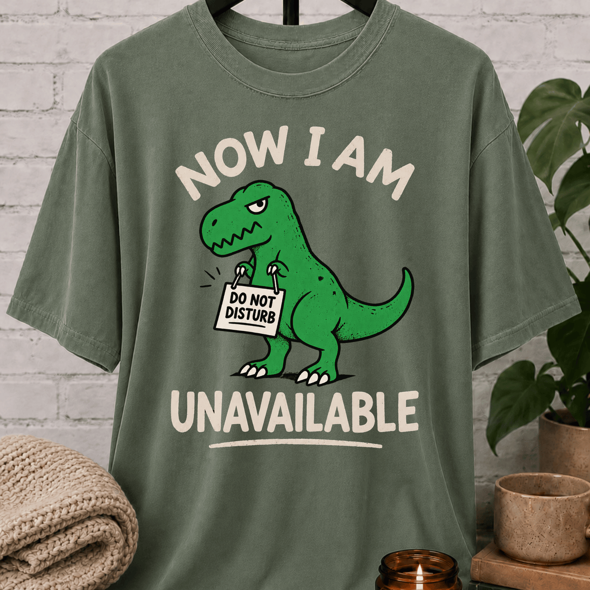 Funny dinosaur T-shirt featuring a green T-rex holding a “Do Not Disturb” sign with the phrase “Now I Am Unavailable,” a sarcastic loner graphic tee for hermits, socially unavailable types, and personal space humor fans.