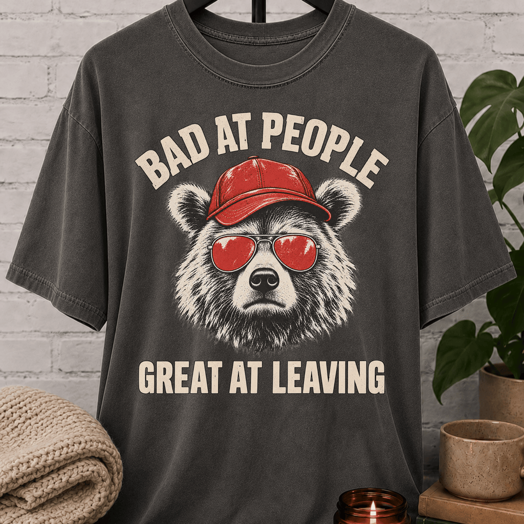Socially awkward bear T-shirt featuring a bear in sunglasses and a red cap with the phrase “Bad at People Great at Leaving,” a sarcastic graphic tee for people who hate small talk and leave early.