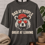 Socially awkward bear T-shirt featuring a bear in sunglasses and a red cap with the phrase “Bad at People Great at Leaving,” a sarcastic graphic tee for people who hate small talk and leave early.