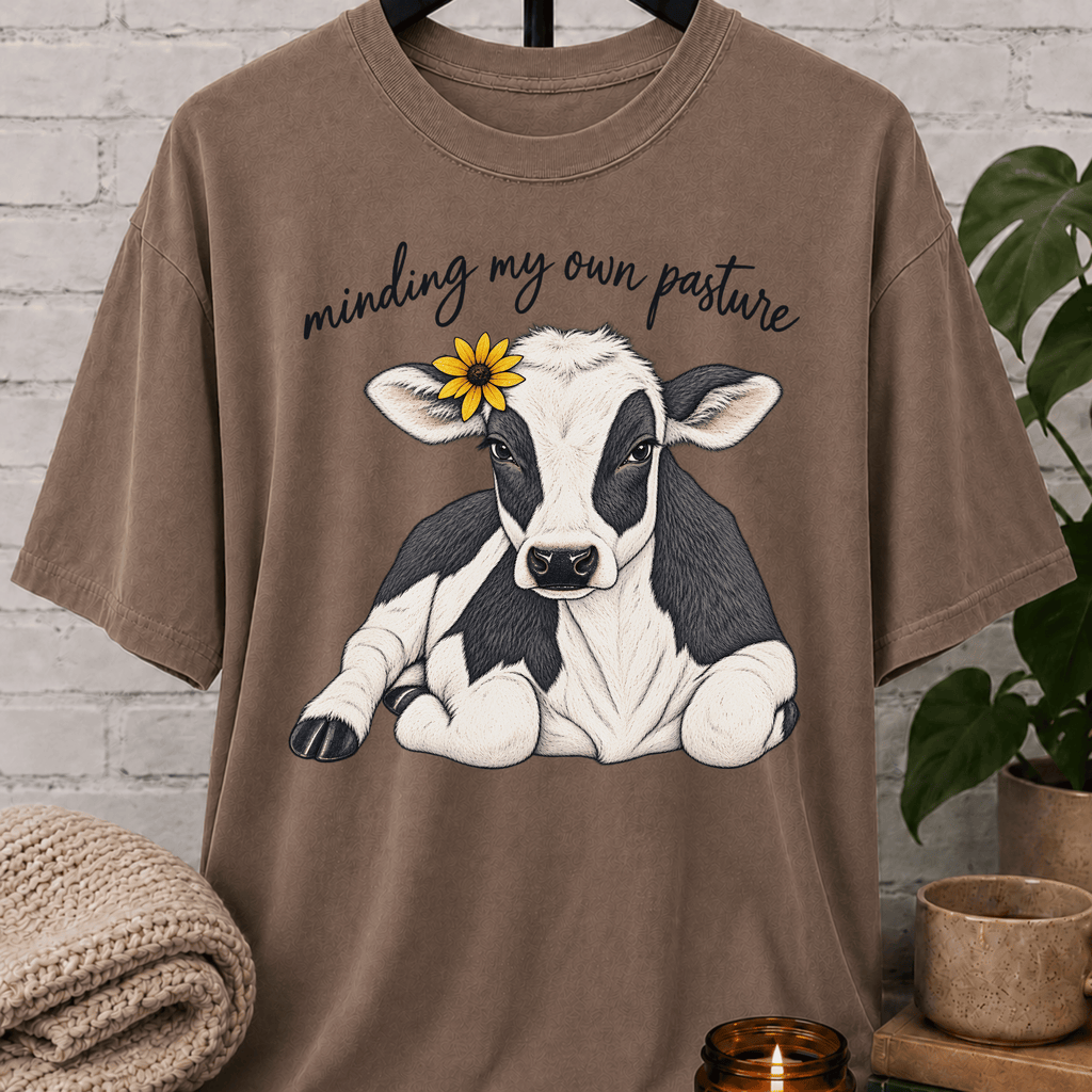 Cow graphic T-shirt featuring a black and white calf with a sunflower and the phrase “Minding My Own Pasture,” a sarcastic personal space shirt for people who keep to themselves and enjoy farm animal humor.