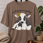 Cow graphic T-shirt featuring a black and white calf with a sunflower and the phrase “Minding My Own Pasture,” a sarcastic personal space shirt for people who keep to themselves and enjoy farm animal humor.