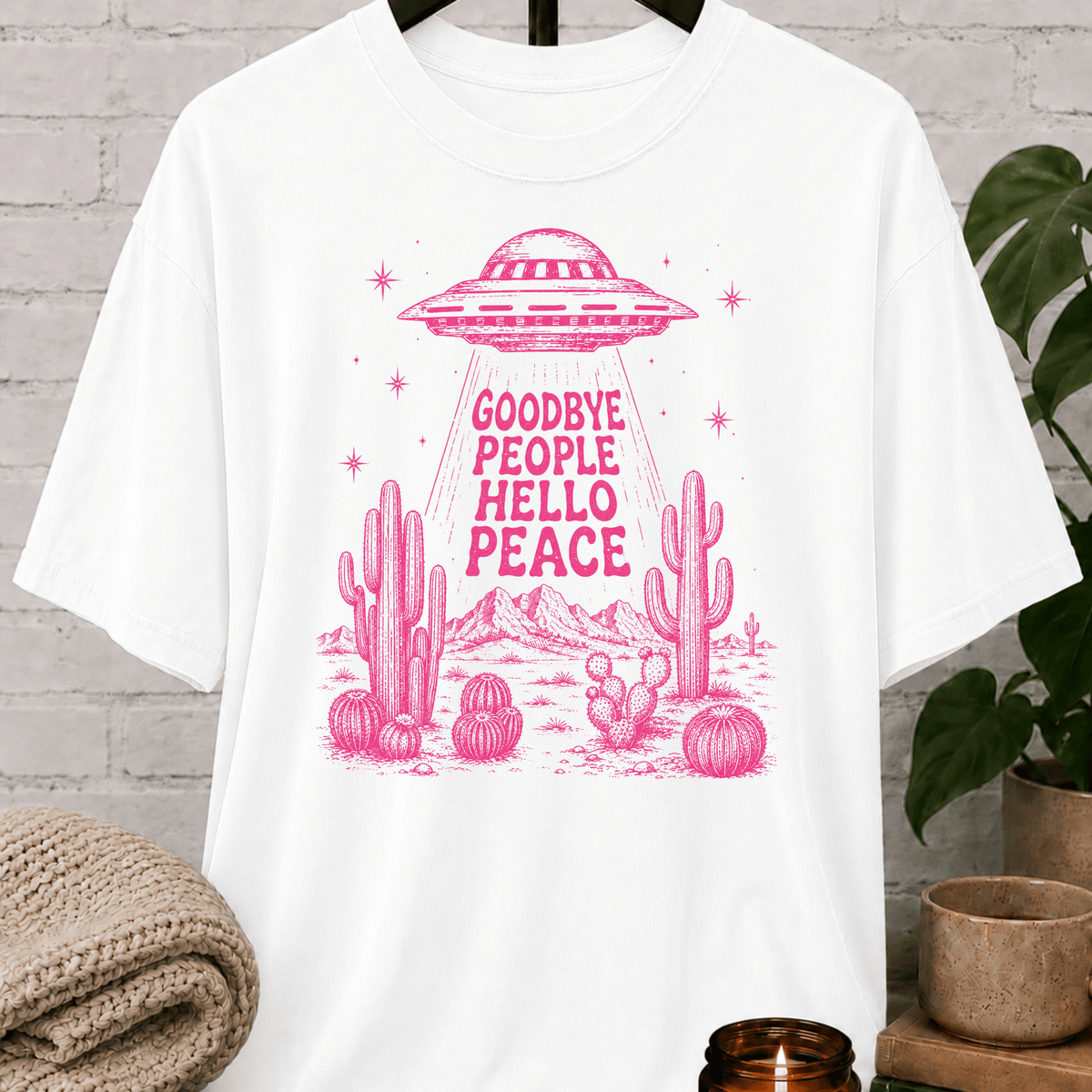 Antisocial alien UFO T-shirt featuring a pink flying saucer hovering above desert cacti with the phrase “Goodbye People Hello Peace,” a sarcastic graphic tee for loners and people who prefer solitude.