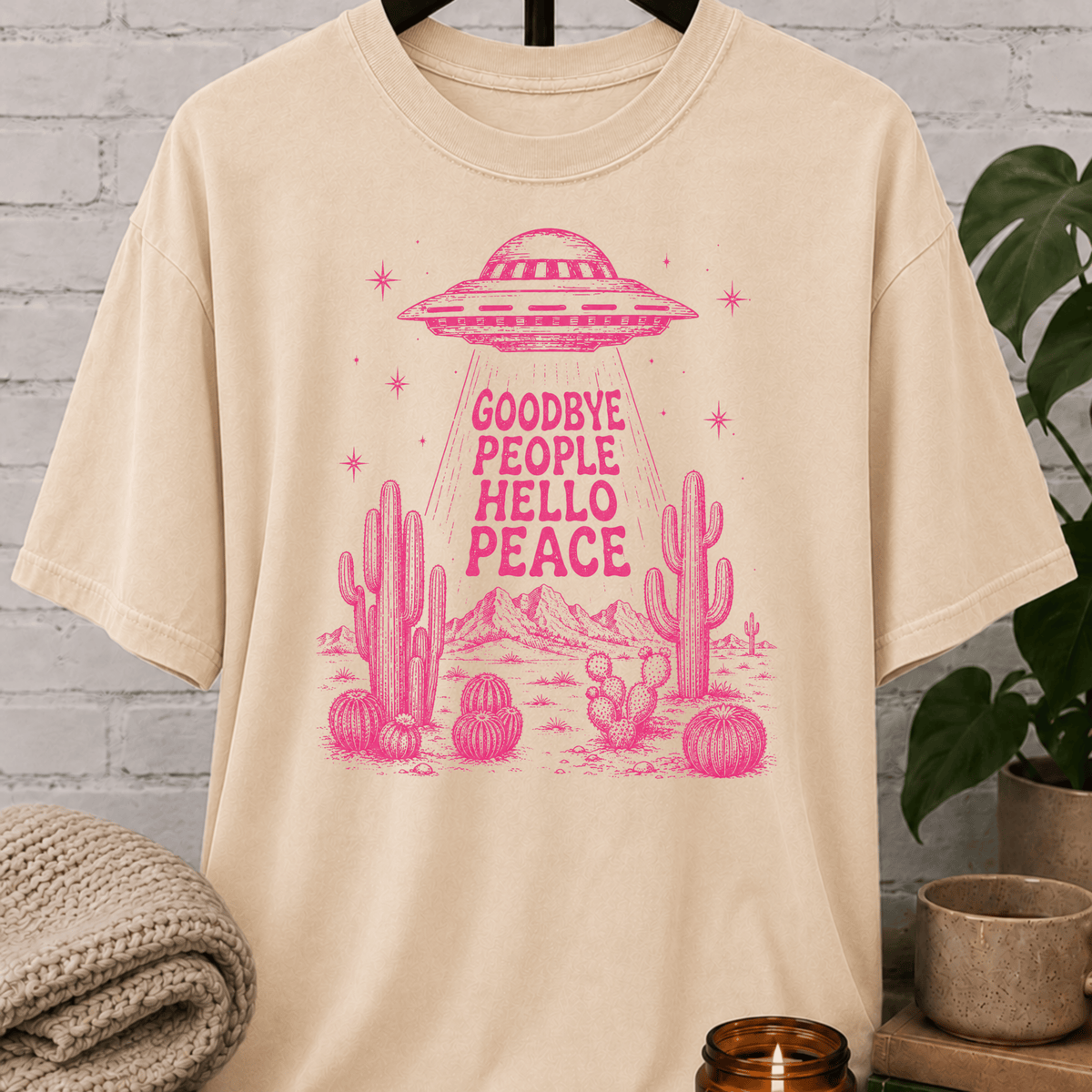 Antisocial alien UFO T-shirt featuring a pink flying saucer hovering above desert cacti with the phrase “Goodbye People Hello Peace,” a sarcastic graphic tee for loners and people who prefer solitude.
