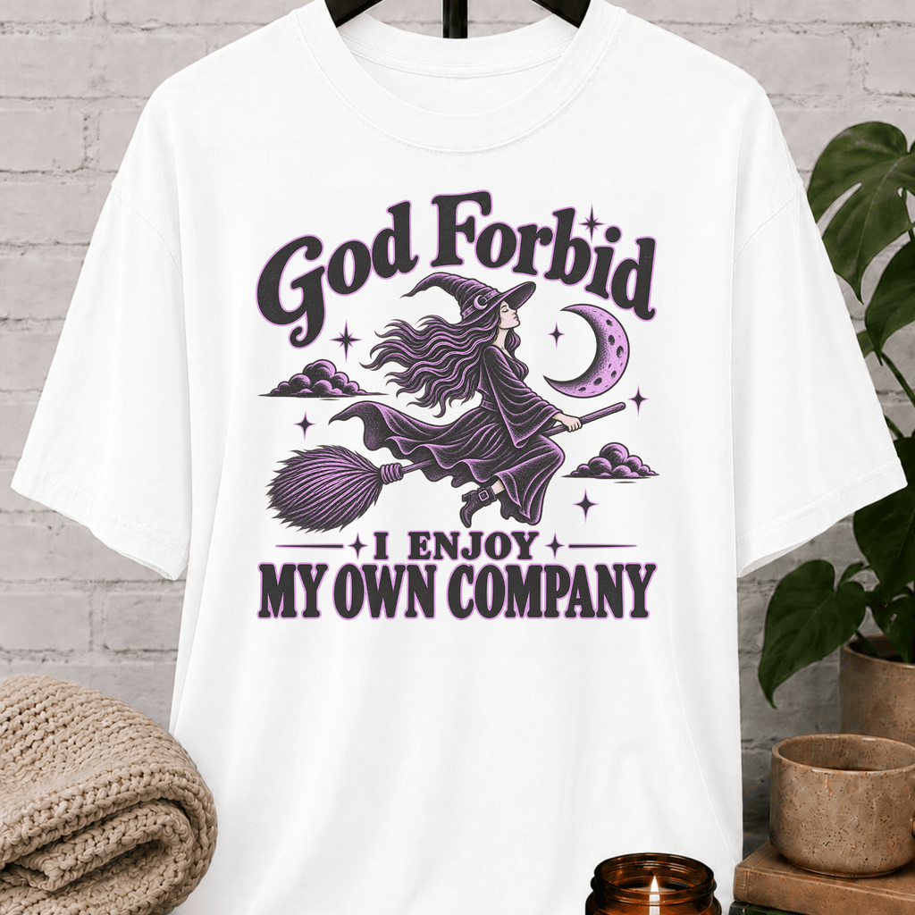 Witch graphic T-shirt featuring a flying witch on a broom, crescent moon, stars, and the phrase “God Forbid I Enjoy My Own Company,” a sarcastic solitude shirt for loners and independent people.
