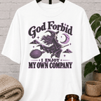 Witch graphic T-shirt featuring a flying witch on a broom, crescent moon, stars, and the phrase “God Forbid I Enjoy My Own Company,” a sarcastic solitude shirt for loners and independent people.