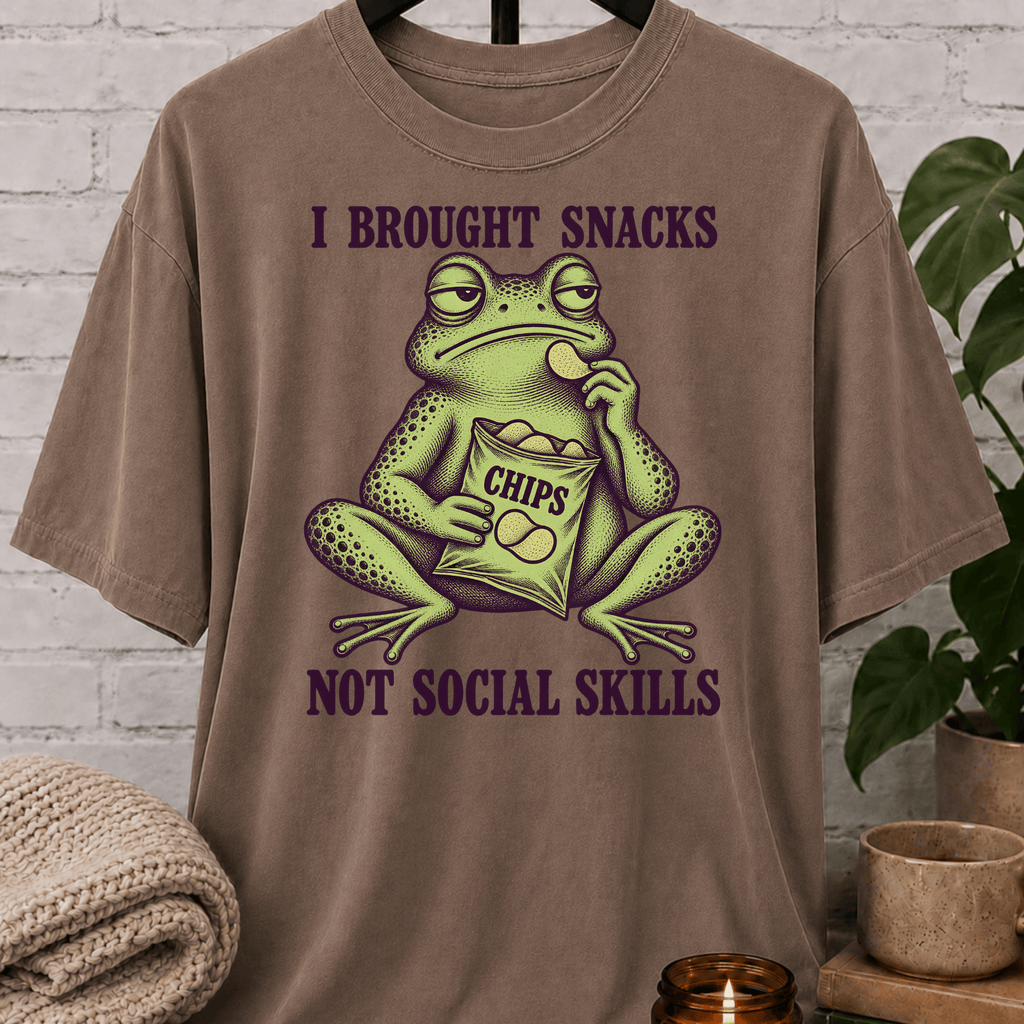 Socially awkward frog graphic T-shirt featuring an unimpressed green frog eating chips with the phrase “I Brought Snacks Not Social Skills,” a sarcastic snack humor shirt for awkward people and low social battery types.