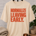 Socially selective graphic T-shirt featuring bold distressed lettering that reads “Normalize Leaving Early,” a sarcastic leave-early shirt for low social battery days and people who prefer an early exit.