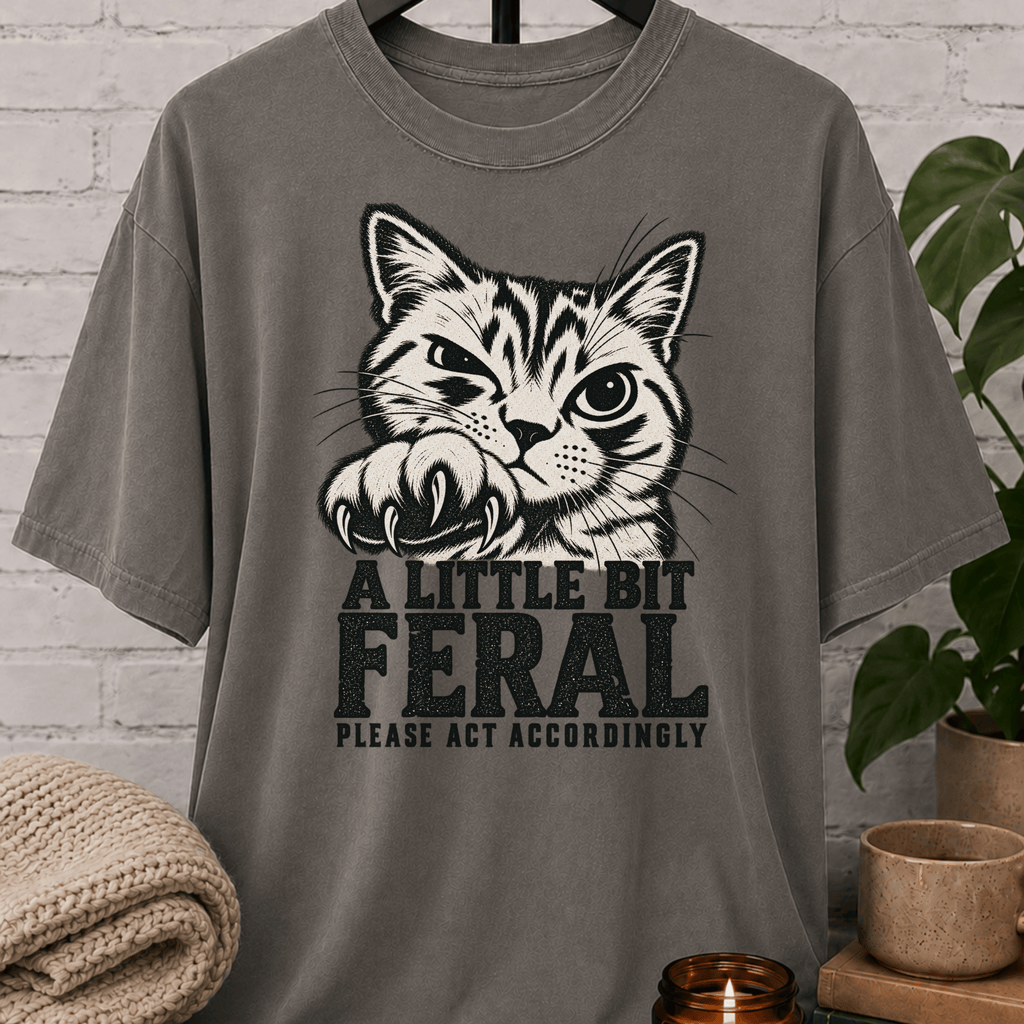 Sarcastic cat graphic T-shirt featuring a clawing tabby cat with the phrase “A Little Bit Feral Please Act Accordingly,” a funny cat lover shirt for socially selective people and antisocial humor fans.