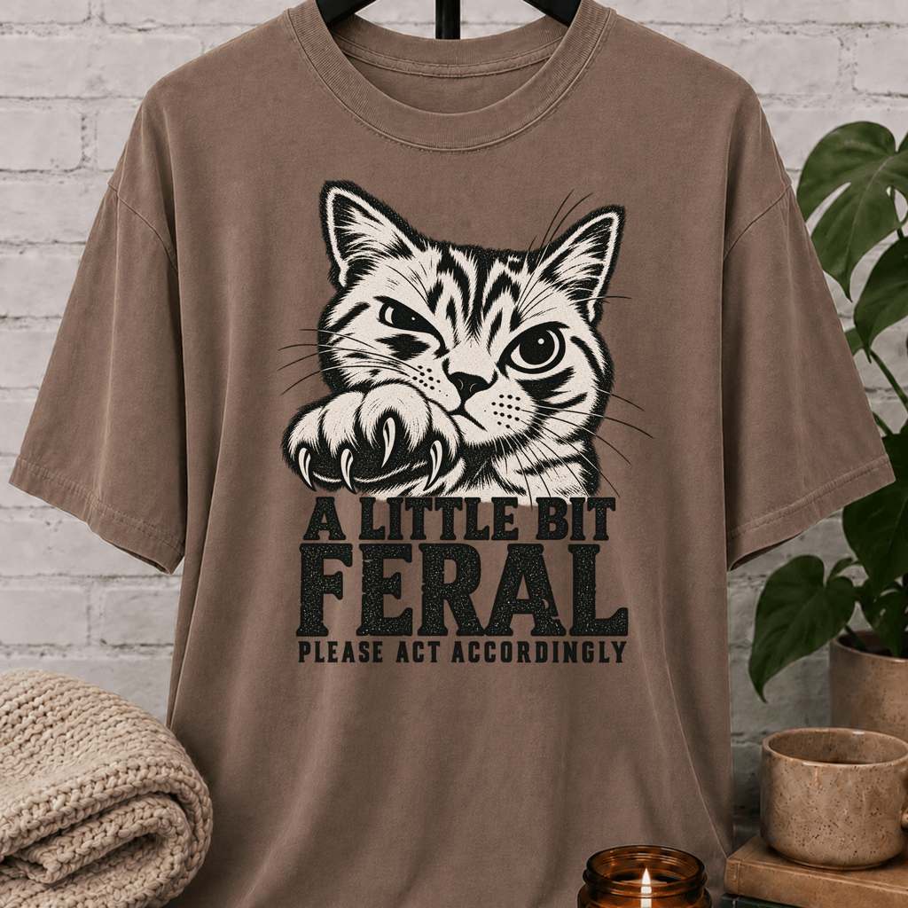 Sarcastic cat graphic T-shirt featuring a clawing tabby cat with the phrase “A Little Bit Feral Please Act Accordingly,” a funny cat lover shirt for socially selective people and antisocial humor fans.
