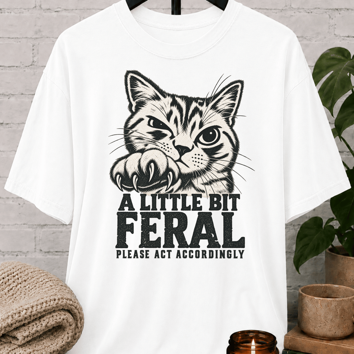 Sarcastic cat graphic T-shirt featuring a clawing tabby cat with the phrase “A Little Bit Feral Please Act Accordingly,” a funny cat lover shirt for socially selective people and antisocial humor fans.