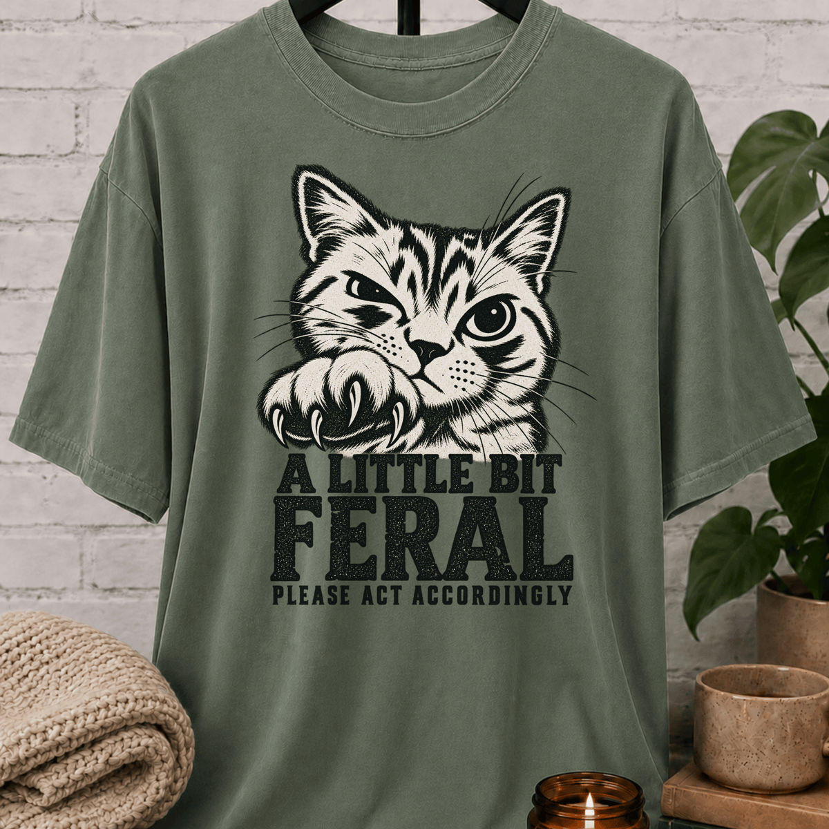 Sarcastic cat graphic T-shirt featuring a clawing tabby cat with the phrase “A Little Bit Feral Please Act Accordingly,” a funny cat lover shirt for socially selective people and antisocial humor fans.