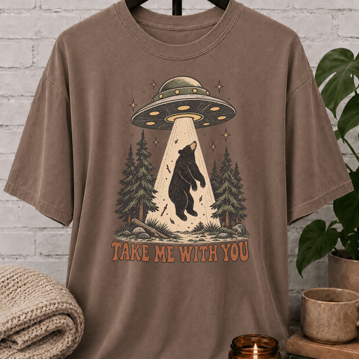 UFO bear graphic T-shirt featuring a black bear being abducted by a flying saucer above a pine forest with the phrase “Take Me With You,” an alien abduction shirt for loners, solitude lovers, and people-avoidance humor fans.