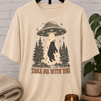 UFO bear graphic T-shirt featuring a black bear being abducted by a flying saucer above a pine forest with the phrase “Take Me With You,” an alien abduction shirt for loners, solitude lovers, and people-avoidance humor fans.