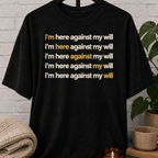 Social obligation graphic T-shirt featuring the repeated phrase “I’m Here Against My Will,” a sarcastic shirt for reluctant attendees, socially selective people, and fans of unwanted plans humor.