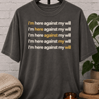 Social obligation graphic T-shirt featuring the repeated phrase “I’m Here Against My Will,” a sarcastic shirt for reluctant attendees, socially selective people, and fans of unwanted plans humor.