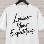 Lower Your Expectations graphic T-shirt featuring bold handwritten lettering, a blunt humor shirt for low-expectation personalities, sarcastic humor fans, and people who prefer keeping the bar low.