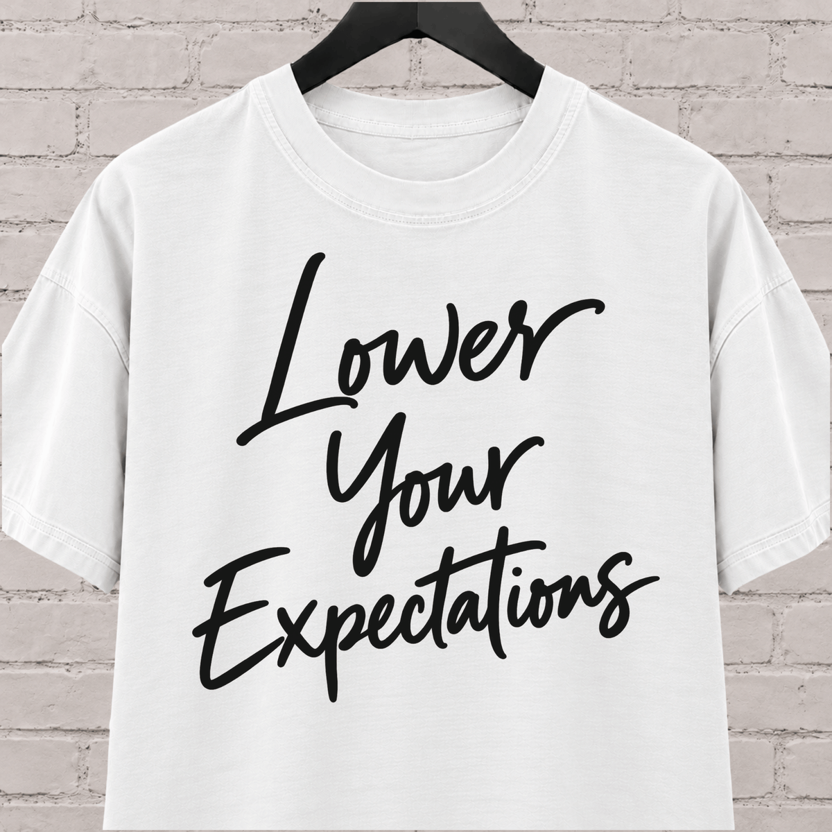 Lower Your Expectations graphic T-shirt featuring bold handwritten lettering, a blunt humor shirt for low-expectation personalities, sarcastic humor fans, and people who prefer keeping the bar low.