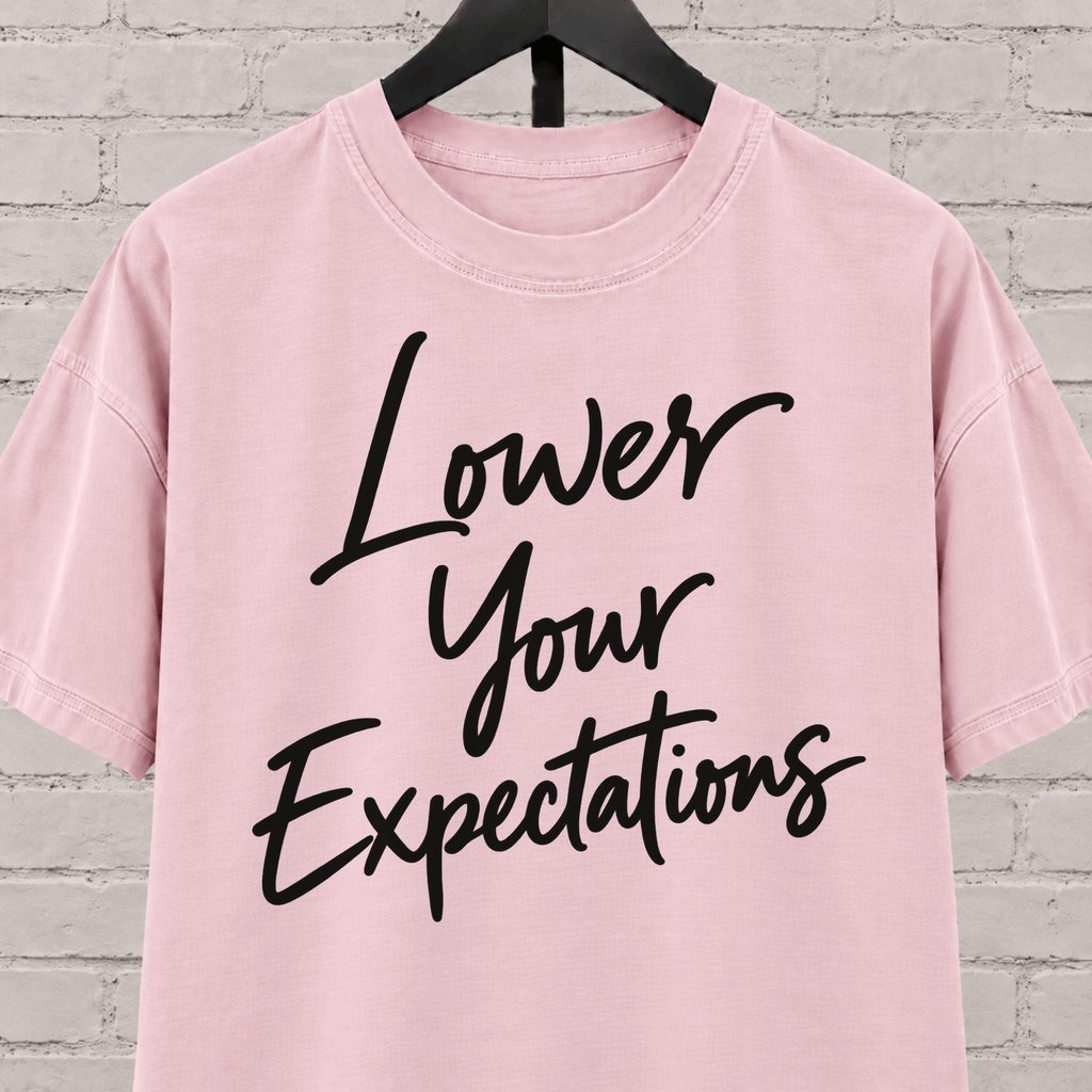 Lower Your Expectations graphic T-shirt featuring bold handwritten lettering, a blunt humor shirt for low-expectation personalities, sarcastic humor fans, and people who prefer keeping the bar low.