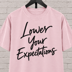Lower Your Expectations graphic T-shirt featuring bold handwritten lettering, a blunt humor shirt for low-expectation personalities, sarcastic humor fans, and people who prefer keeping the bar low.