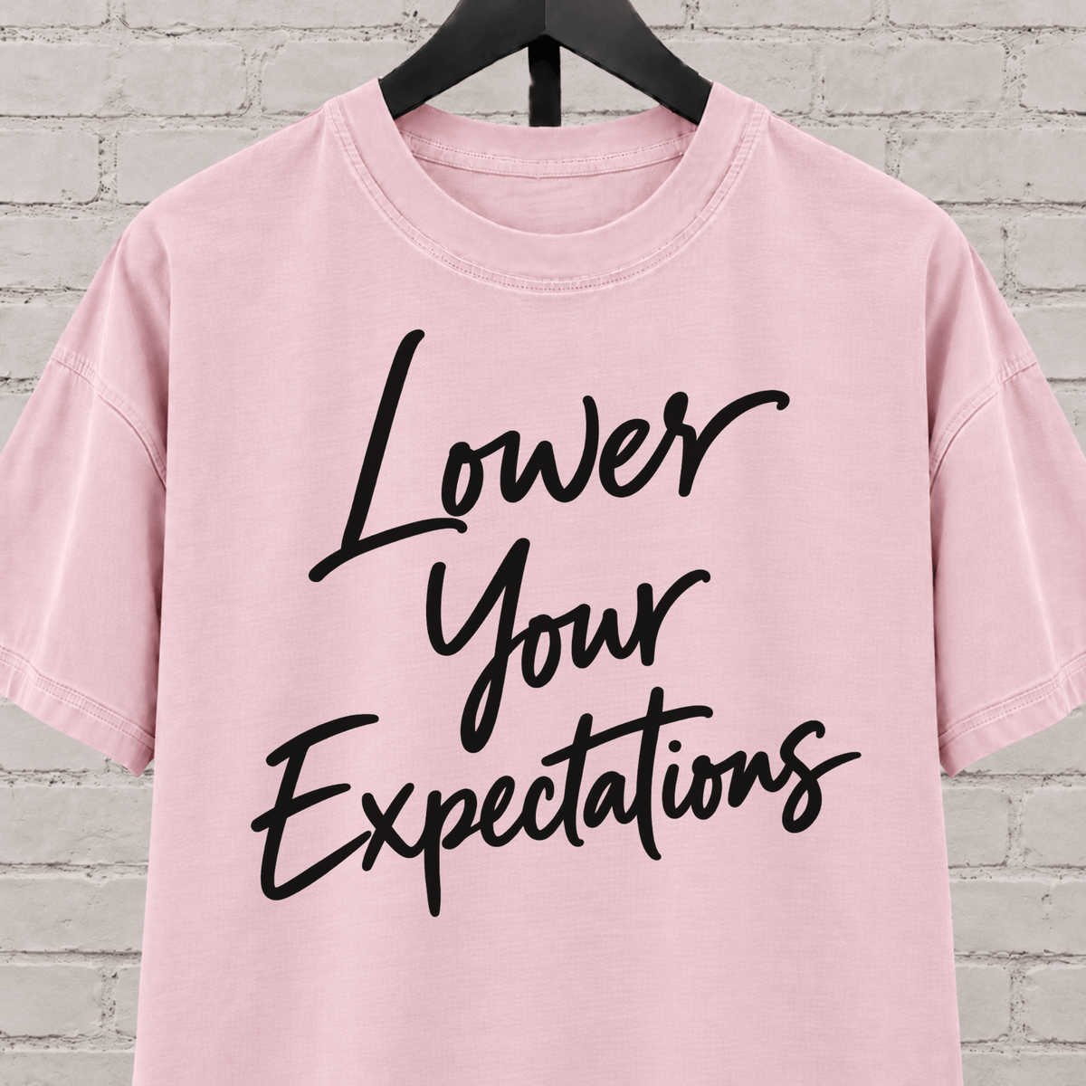 Lower Your Expectations graphic T-shirt featuring bold handwritten lettering, a blunt humor shirt for low-expectation personalities, sarcastic humor fans, and people who prefer keeping the bar low.