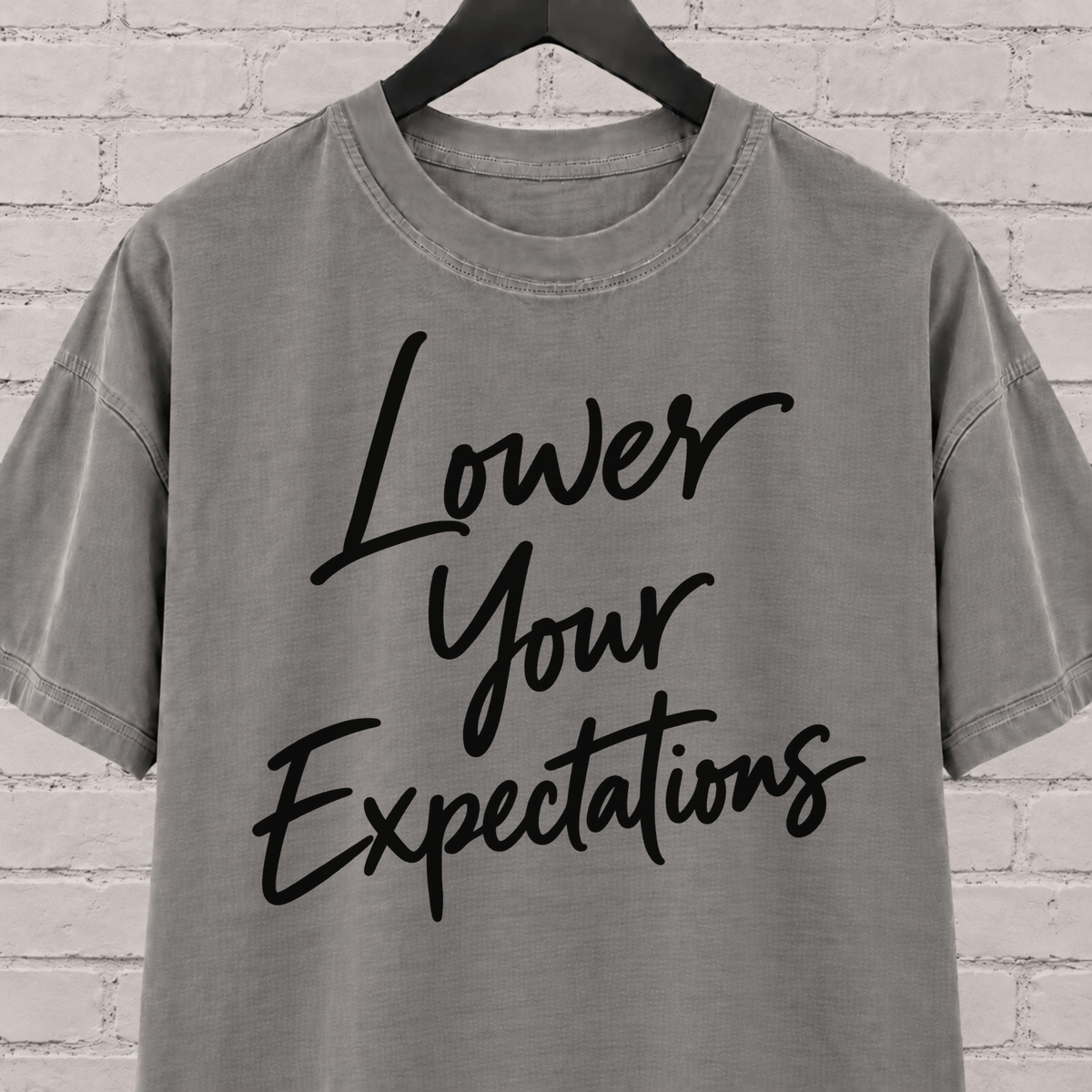 Lower Your Expectations graphic T-shirt featuring bold handwritten lettering, a blunt humor shirt for low-expectation personalities, sarcastic humor fans, and people who prefer keeping the bar low.