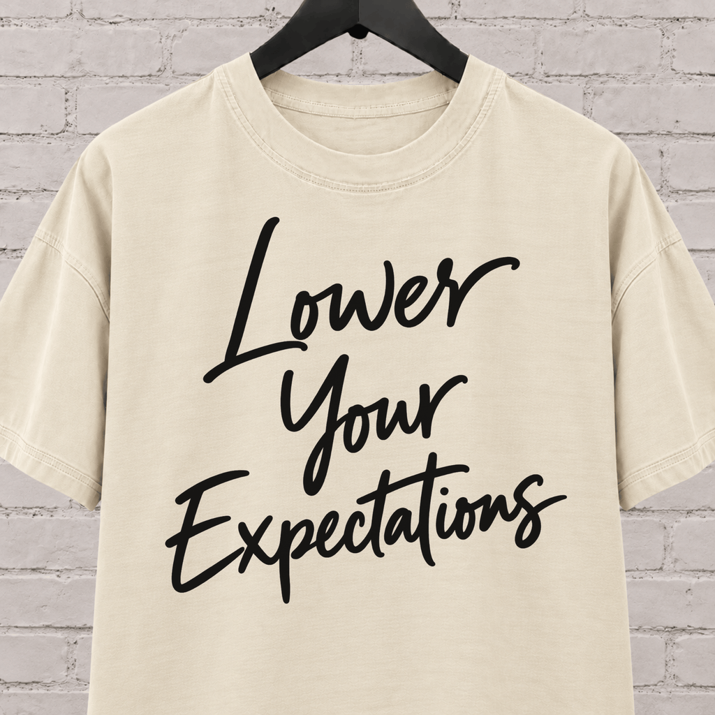 Lower Your Expectations graphic T-shirt featuring bold handwritten lettering, a blunt humor shirt for low-expectation personalities, sarcastic humor fans, and people who prefer keeping the bar low.