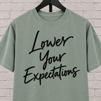 Lower Your Expectations graphic T-shirt featuring bold handwritten lettering, a blunt humor shirt for low-expectation personalities, sarcastic humor fans, and people who prefer keeping the bar low.