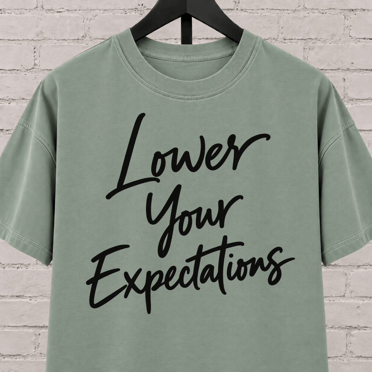 Lower Your Expectations graphic T-shirt featuring bold handwritten lettering, a blunt humor shirt for low-expectation personalities, sarcastic humor fans, and people who prefer keeping the bar low.