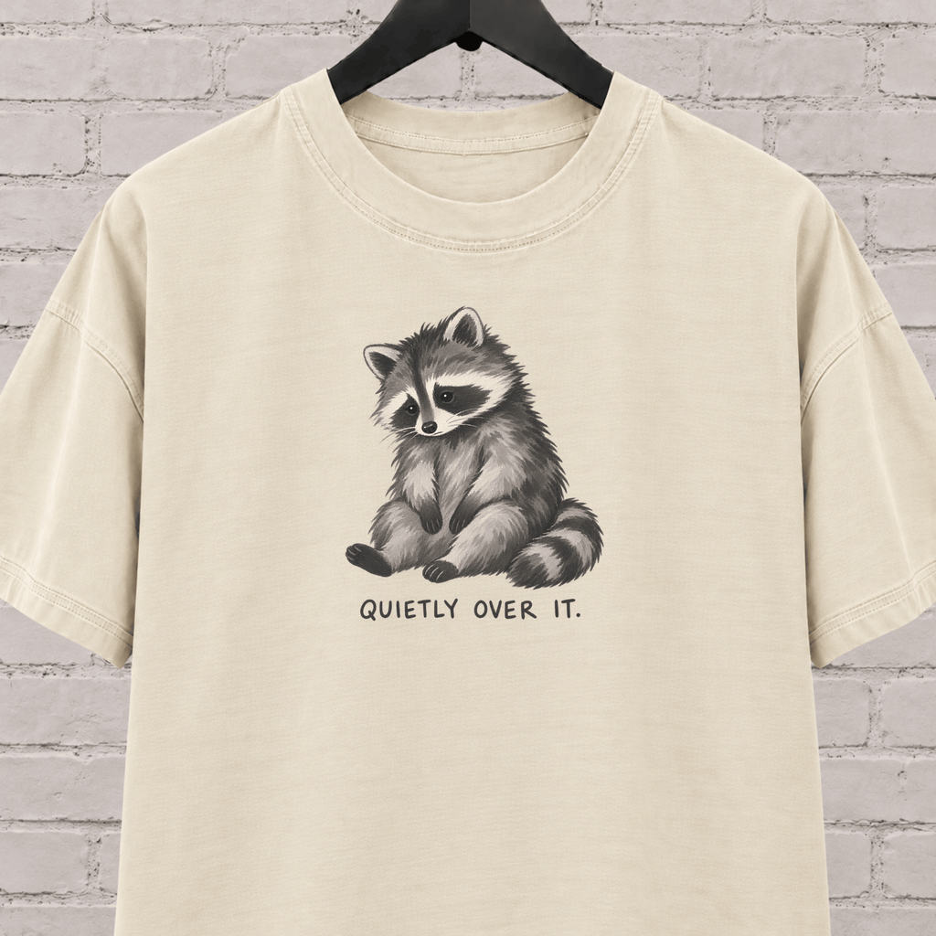 Quietly Over It raccoon graphic T-shirt featuring a tired raccoon, a low social battery shirt for socially drained people and introvert humor fans.