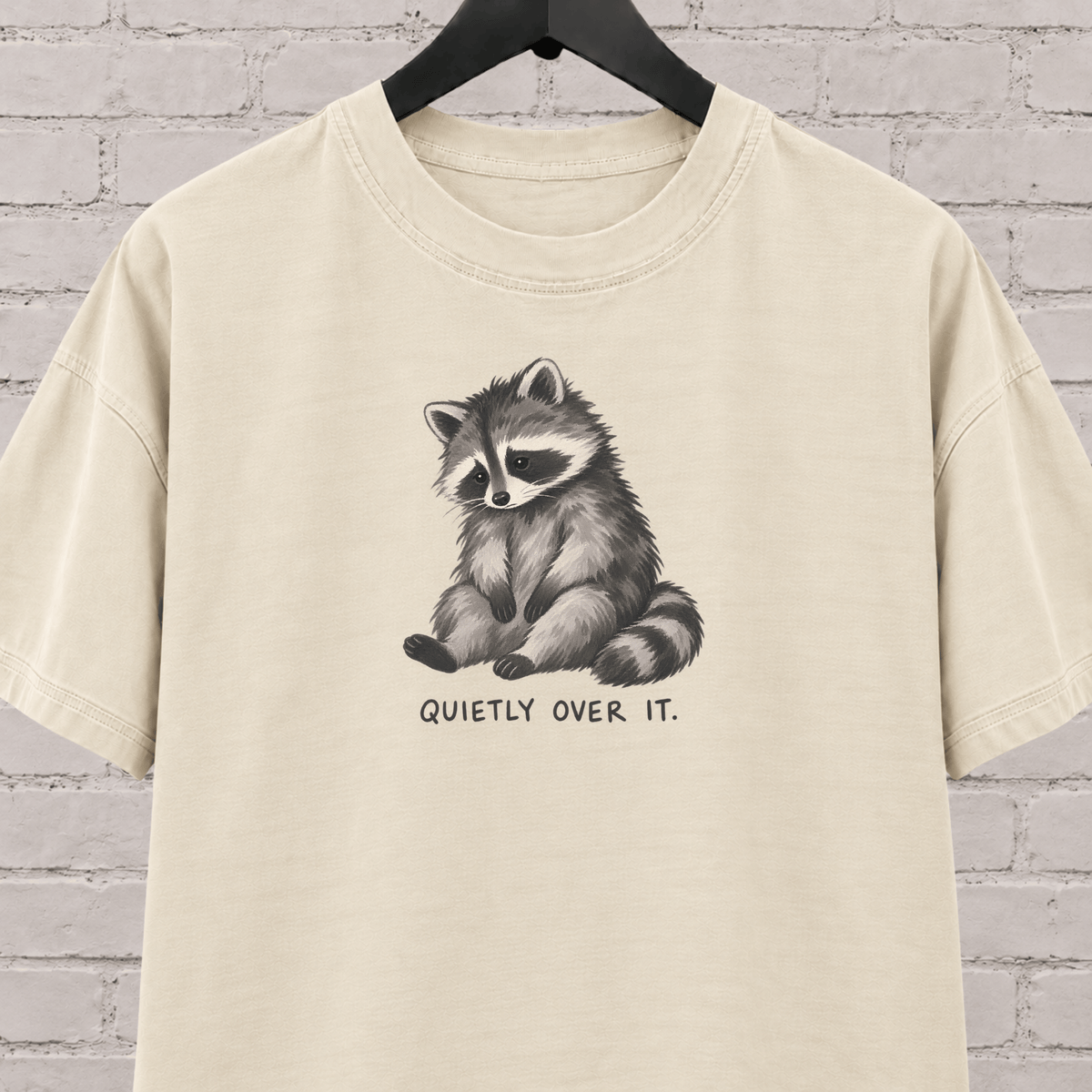 Quietly Over It raccoon graphic T-shirt featuring a tired raccoon, a low social battery shirt for socially drained people and introvert humor fans.