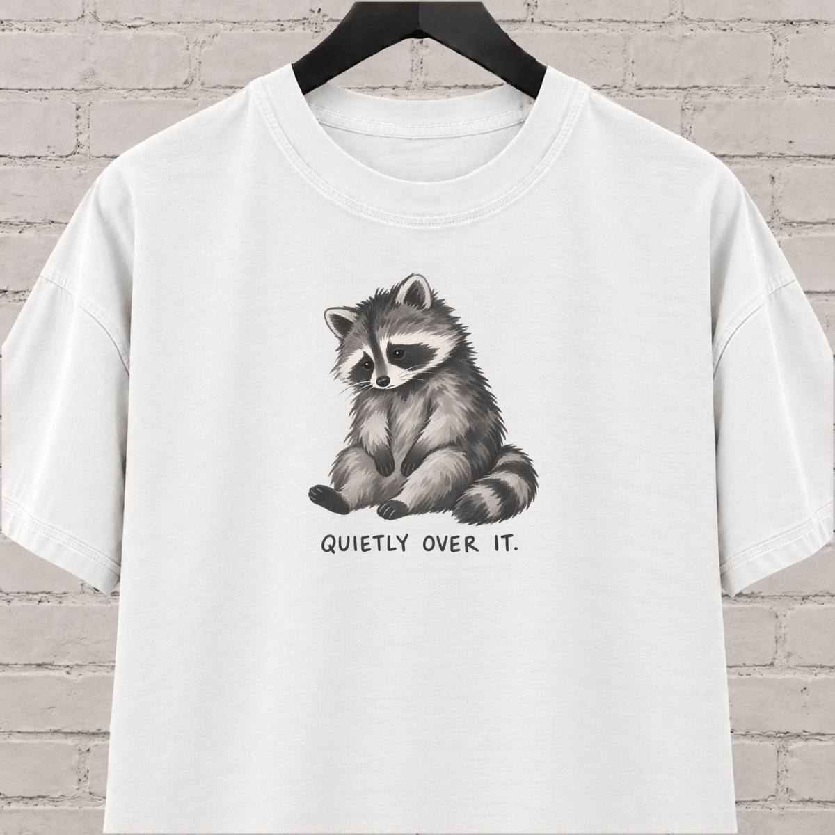 Quietly Over It raccoon graphic T-shirt featuring a tired raccoon, a low social battery shirt for socially drained people and introvert humor fans.